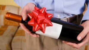 Egy férfi kezében egy ajándékba szánt borosüveg, piros masnival díszítve.