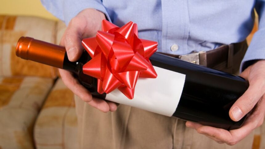 Egy férfi kezében egy ajándékba szánt borosüveg, piros masnival díszítve.
