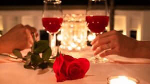 womensway 144 Két pohár vörös ital és egy vörös rózsa egy romantikus asztalon, gyertyafénynél.