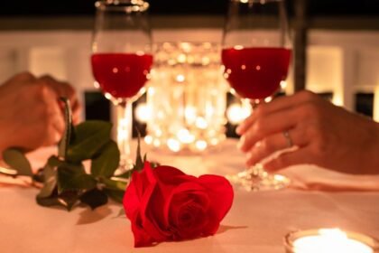 Két pohár vörös ital és egy vörös rózsa egy romantikus asztalon, gyertyafénynél.