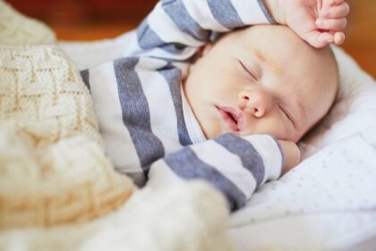 Egy kisbaba békésen alszik, csíkos ruhában, puha takaró alatt.