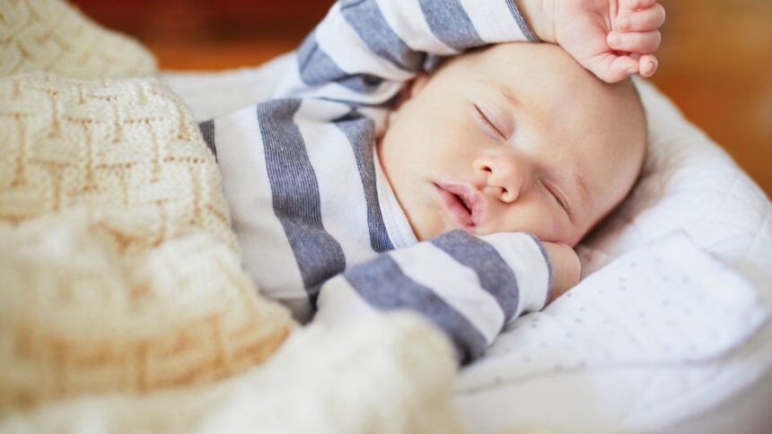 Egy kisbaba békésen alszik, csíkos ruhában, puha takaró alatt.