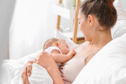 Egy édesanya szoptatja a babáját, miközben kényelmesen ül az ágyon.