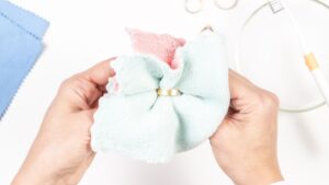 Két kéz egy arany gyűrűt tisztít egy színes mikroszálas kendőben, háttérben tisztító eszközök.