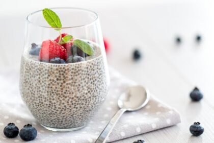 Egy pohár chia mag puding friss gyümölcsökkel, mint málna és áfonya, egy fehér terítőn.