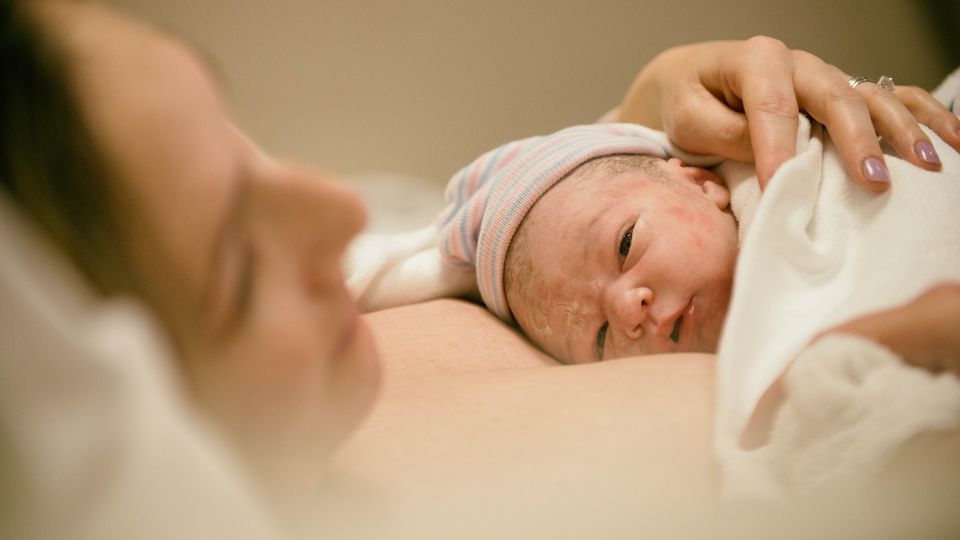 Egy újszülött baba anyja karjaiban, boldog pillanatban, kórházi környezetben.