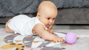 womensway 136 Egy kisbaba hason fekszik a szőnyegen, és egy lila labdát próbál elérni.