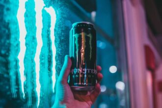 Egy kézben tartott Monster energiaital doboza, háttérben neonfényekkel.