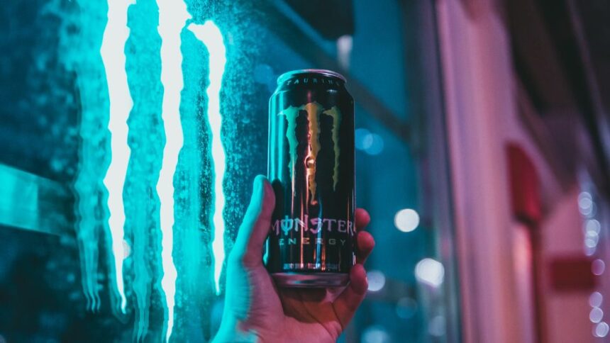 Egy kézben tartott Monster energiaital doboza, háttérben neonfényekkel.