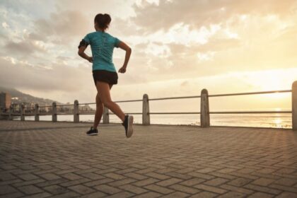 Egy fiatal nő fut a tengerparti sétányon, napfelkeltében, energikus mozdulattal.