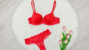 Piros csipkés melltartó és tanga egy fehér szőnyegen, mellette virágokkal.