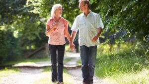 Két idős ember sétál együtt egy napfényes, zöld parkban, boldogan beszélgetve.