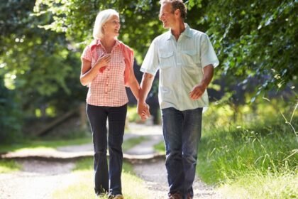 Két idős ember sétál együtt egy napfényes, zöld parkban, boldogan beszélgetve.