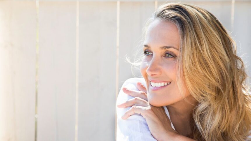 40 feletti nők gyakran ezeket a hibákat követik el a randiappokon 1 Egy mosolygó nő, aki a kezét az állán támasztja, vidám és magabiztos megjelenéssel.