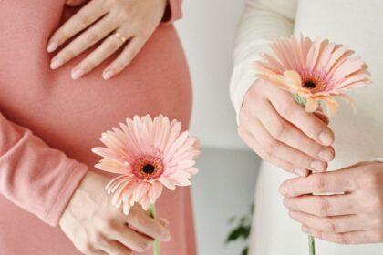 Két várandós nő, akik virágokat tartanak a kezükben, egyikük keze a hasán pihen.