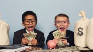 womensway 126 Két kisfiú öltönyben, boldogan tartanak pénzt és mosolyognak, mögöttük pénzeszsákok.