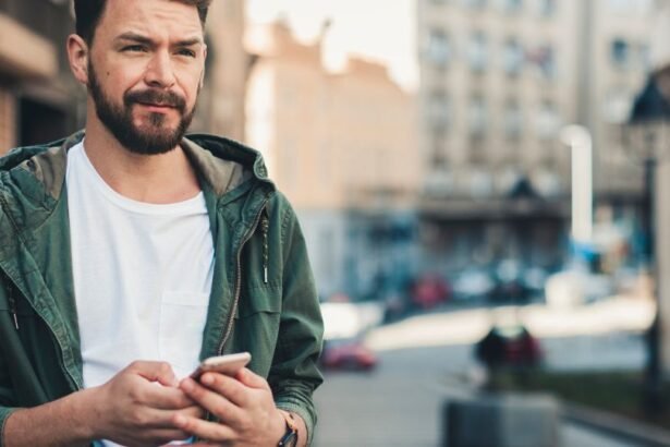 Egy fiatal férfi áll az utcán, kezében okostelefonnal, gondolkodó arckifejezéssel.