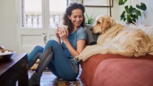 Egy fiatal nő ül a padlón, kezében egy csésze, mellette egy arany retriever pihen.