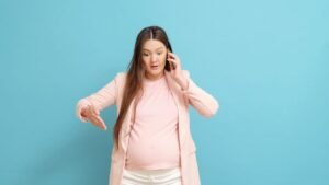 Egy várandós nő telefonál, miközben aggódva néz lefelé, jelezve a magzatvíz szivárgásának lehetőségét.