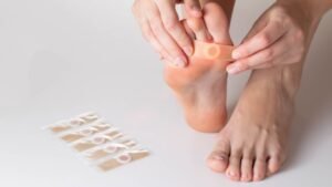 Egy női láb, amelyen egy tapasz van, a talpon, a háttérben tapaszcsomagokkal.