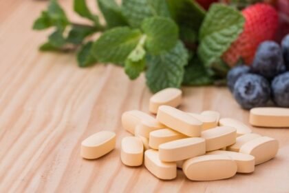 Sárga multivitamin tabletták friss gyümölcsök, például eper és áfonya mellett.