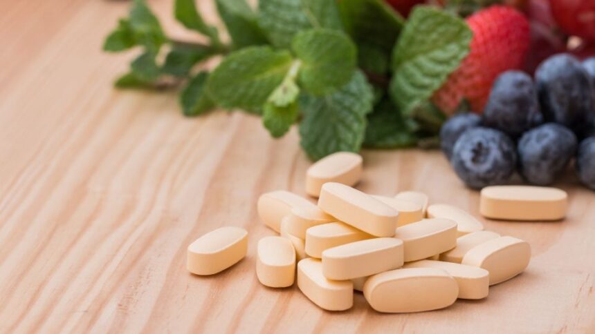 Sárga multivitamin tabletták friss gyümölcsök, például eper és áfonya mellett.