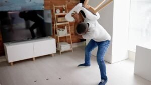 Egy férfi egy széket emel a levegőben, miközben csótányokat próbál eltávolítani a lakásban.