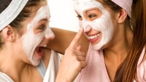 Két fiatal lány arcpakolást visel, vidáman nevetnek és játszanak egymással.