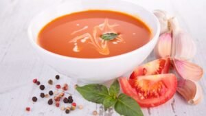 Friss, ízletes paradicsomleves tálalva, körülötte friss paradicsom és fokhagyma.
