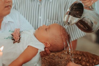 Egy kisbaba keresztelője, ahol víz ömlik a fejére, miközben a szülők és a pap jelen vannak.