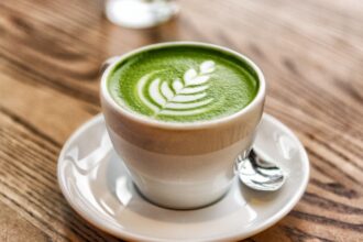 Egy csésze matcha tea, zöld színű, levelekkel díszítve, fehér alátéttel.