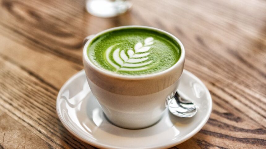 Egy csésze matcha tea, zöld színű, levelekkel díszítve, fehér alátéttel.