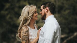 Egy fiatal nő és egy idősebb férfi közel állnak egymáshoz, mosolyognak, romantikus pillanatot osztanak meg.