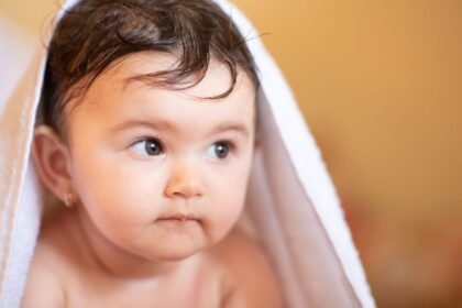 Egy újszülött, akit törölköző takar, figyelmesen néz előre, miközben a háttér homályos.