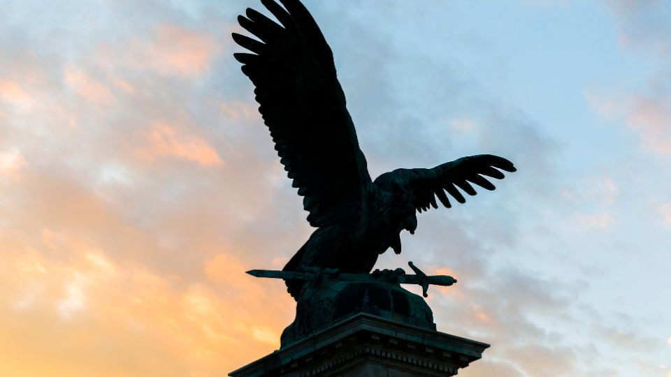 Egy hatalmas, szárnyait kitáró sas szobra, amely a naplementében áll, szimbolizálva a védelmet és a bátorságot.