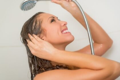 Egy nő boldogan zuhanyzik, miközben a víz csorog a hajára, frissítő érzést keltve.