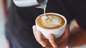 womensway 128 Egy kéz egy fehér csészében kávét önt, a kávé tetején szép latte art látható.