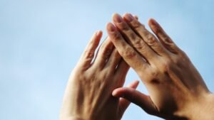 Két kéz, amely egymásra van helyezve, a háttérben világos égbolt látható. A körmök egészségesnek tűnnek, de a sötét foltok figyelmeztető jelek lehetnek.