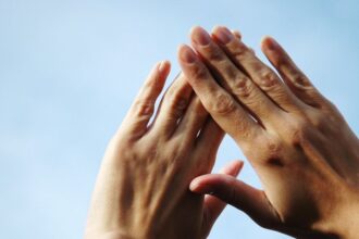 Két kéz, amely egymásra van helyezve, a háttérben világos égbolt látható. A körmök egészségesnek tűnnek, de a sötét foltok figyelmeztető jelek lehetnek.