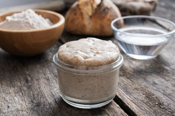 Egy üvegben lévő élesztő, mellette víz és liszt, háttérben kenyér.
