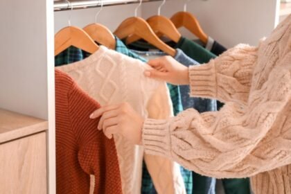 Egy nő éppen egy szekrényből választ ruhát, miközben a polcon különböző színekben és textúrákban lógó pulóverek láthatók.