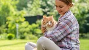 womensway 134 Egy nő boldogan tart a karjában egy narancssárga macskát, miközben zöld környezetben ül.