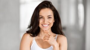 Egy magabiztos nő mosolyog, kezével az állát támasztja, sugárzó önbizalommal.