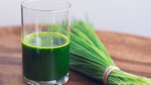 Egy pohár friss zöld búzafűlé, mellette friss búzafű csokor.