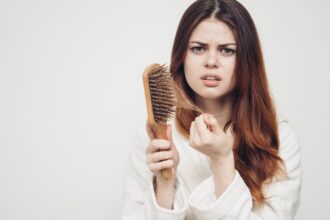 Egy fiatal nő aggódva nézi a hajkefét, amelyen hajszálak vannak.