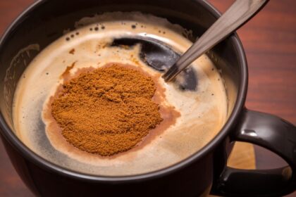 Egy fekete bögre instant kávé, a tetején kávéporral.