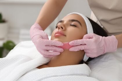 Kozmetikai kezelés során egy nő arcbőrét ápolják, rózsaszín kesztyűben.