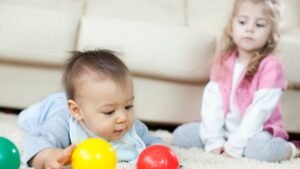 womensway 132 Egy kisbaba játszik színes labdákkal, míg a nővére figyeli.