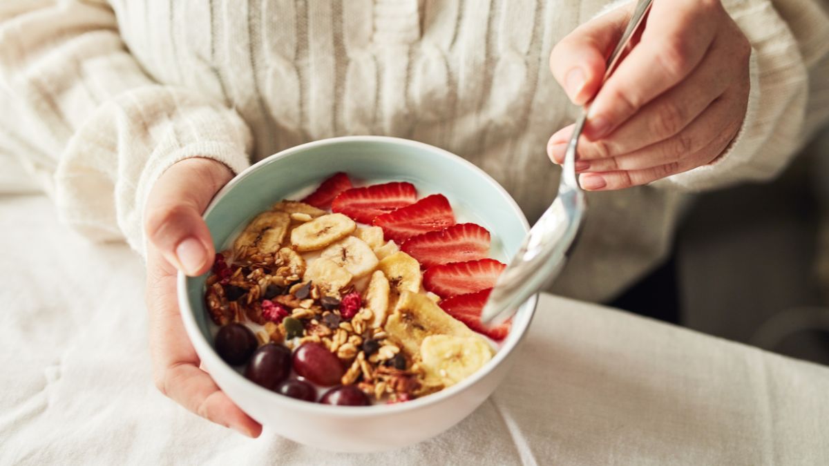 Egy tálban joghurt, granola, gyümölcsök és diófélék láthatók, egészséges reggeli.