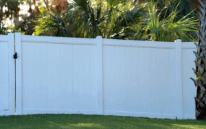 Fehér kerítés zöld fűvel és trópusi növényekkel körülvéve.